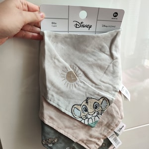 Puede incluir: Un conjunto de tres baberos para bebé con temática de El Rey León. Los baberos están hechos de tela suave y absorbente, perfectos para mantener la ropa del bebé limpia durante las comidas. Los baberos están decorados con un lindo personaje de león y un gráfico de sol. El empaque dice "Disney Home" y "Bibs 3 pack".