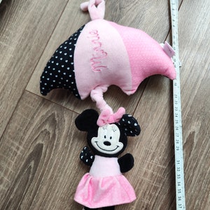 K&ouml;nnte beinhalten: Rosa und schwarzes Pl&uuml;sch-Minnie-Maus-Spielzeug mit einem rosa und schwarzen, gepunkteten Regenschirm. Der Regenschirm ist mit dem Namen "Minnie" bestickt.