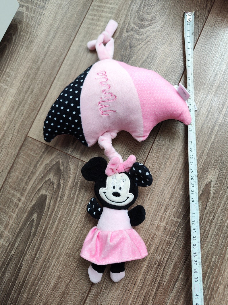 K&ouml;nnte beinhalten: Rosa und schwarzes Pl&uuml;sch-Minnie-Maus-Spielzeug mit einem rosa und schwarzen, gepunkteten Regenschirm. Der Regenschirm ist mit dem Namen "Minnie" bestickt.
