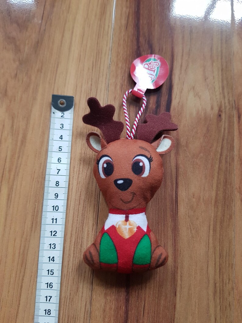May include: A plush reindeer ornament with a red and green outfit, a gold star on its chest, and a red tag that says "Reindeer".
