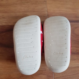 Pu&ograve; includere: Un paio di scarpe rosse per bambini piccoli con pois bianchi. Le scarpe sono della marca Clarks e hanno suole bianche.