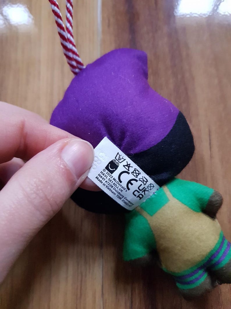 May include: Purple, black, green, and yellow plush toy with a tag that reads "2022 McDonald's, HAVI, SE18DJ, UK, CE, UK, CA, HAVI 47228 Duisburg Germany, Made in Vietnam TDM 25882-7".
