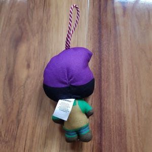 May include: Purple and green plush toy with a black hat and a red and white string attached. The toy has a tag that reads "COLLECTIBLE".