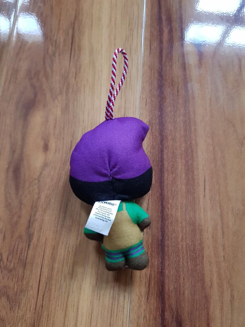 May include: Purple and green plush toy with a black hat and a red and white string attached. The toy has a tag that reads "COLLECTIBLE".