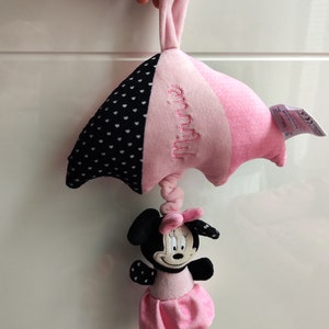 K&ouml;nnte beinhalten: Rosa-schwarzes Babyspielzeug mit einer Minnie Mouse Figur, die an einem rosa-schwarzen Wolkenf&ouml;rmigen Pl&uuml;schtier h&auml;ngt. Die Wolke hat wei&szlig;e Punkte und den Text "Minnie" aufgestickt.