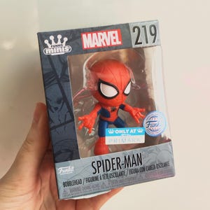 Può includere: Una statuetta bobblehead di Spider-Man Funko Minis in scatola. La statuetta è rossa e blu con occhi bianchi. La scatola presenta il logo Marvel e il numero 219. C'è anche il logo Funko Minis e la scritta "Only at Primark".