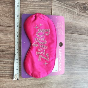 Pu&ograve; includere: Maschera per dormire rosa con la parola "Zzz" in strass. La maschera &egrave; confezionata con una carta bianca che dice "SLEEPING MASK" e "TOMMY HILFIGER" in lettere rosa.