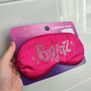 Pu&ograve; includere: Maschera per dormire in raso rosa con la parola "Bratz" in strass. La maschera &egrave; confezionata su una carta viola con le parole "Sleeping Mask" stampate su di essa.
