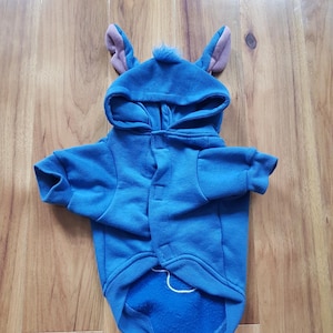 Peut inclure: Un sweat à capuche bleu pour chien avec une capuche ornée d'oreilles et d'une petite touffe de fourrure. Le sweat à capuche pour chien est fait d'une matière douce et possède une fermeture boutonnée. Les oreilles sont bleues avec l'intérieur rose.