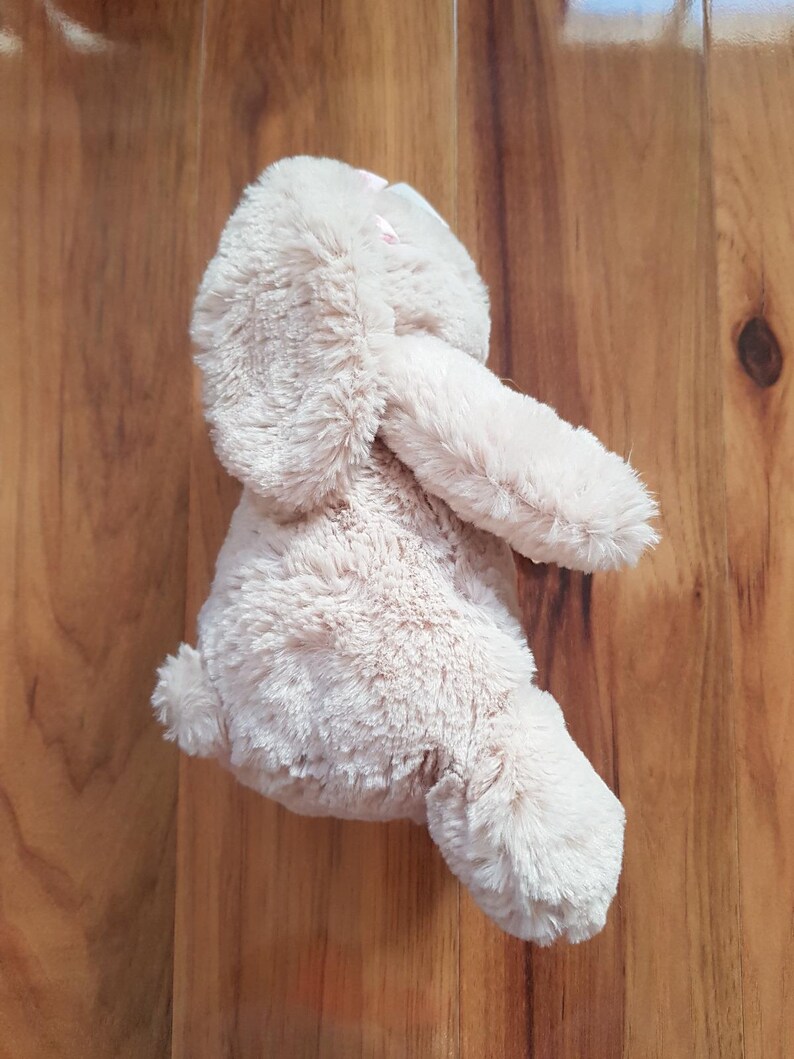 May include: A soft, light brown bunny rabbit toy with long ears and a small, fluffy tail. The bunny is made of a soft, textured material. The toy is designed for children and is suitable for cuddling. The bunny is a light beige colour.