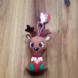May include: A plush reindeer ornament with a red and green outfit and a brown face. The ornament has a red tag with the word "Cheers" on it.