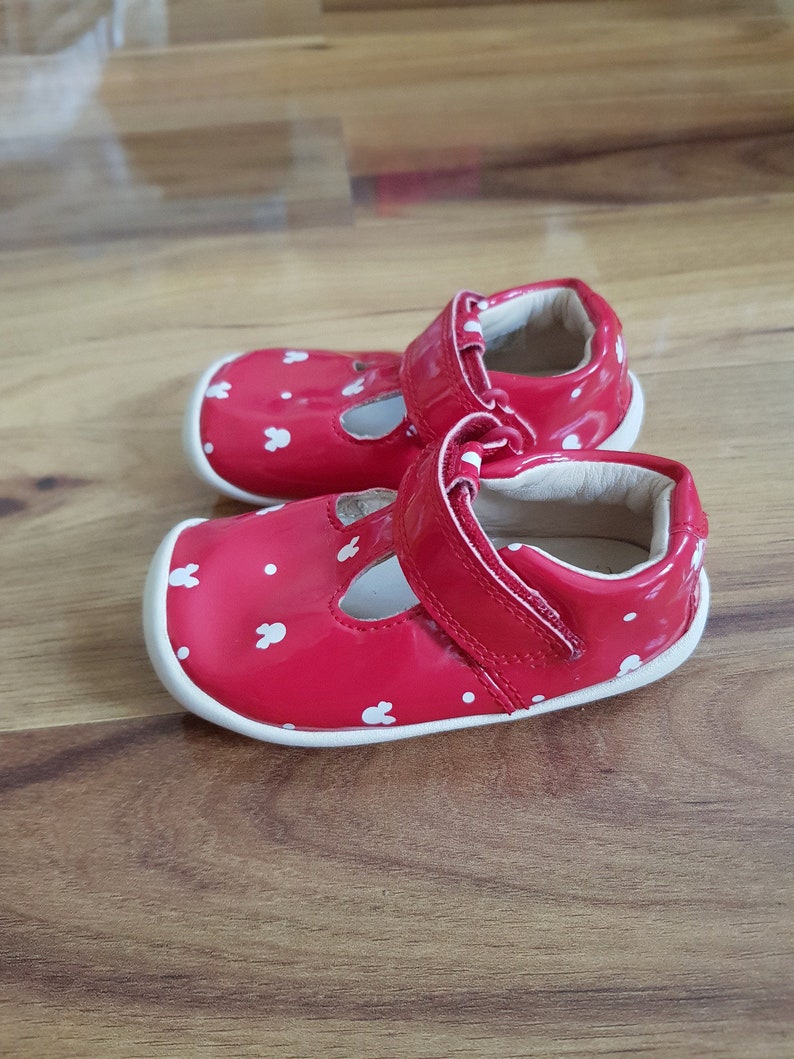 Pu&ograve; includere: Un paio di scarpine da beb&eacute; rosse con pois bianchi e disegni di coniglietti. Le scarpe hanno una suola bianca e un cinturino in velcro.