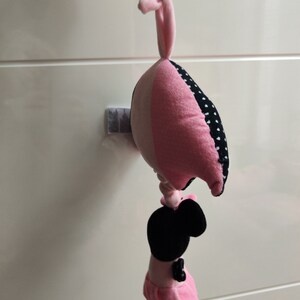 K&ouml;nnte beinhalten: Ein rosa und schwarzes Pl&uuml;schtier mit wei&szlig;em Punktmuster. Das Spielzeug ist herzf&ouml;rmig und hat oben eine Schlaufe zum Aufh&auml;ngen. Ein schwarzes und rosa Pl&uuml;schtier mit schwarzem Gesicht und rosa Kleid ist an der Unterseite des Herzens befestigt.