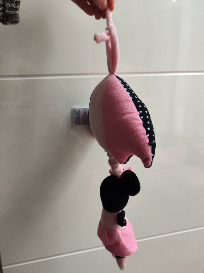 K&ouml;nnte beinhalten: Ein rosa und schwarzes Pl&uuml;schtier mit wei&szlig;em Punktmuster. Das Spielzeug ist herzf&ouml;rmig und hat oben eine Schlaufe zum Aufh&auml;ngen. Ein schwarzes und rosa Pl&uuml;schtier mit schwarzem Gesicht und rosa Kleid ist an der Unterseite des Herzens befestigt.