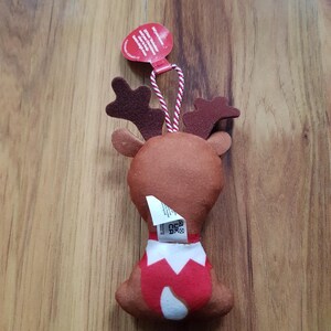 May include: A brown felt reindeer ornament with red antlers and a red and white Santa suit. The ornament has a white tag with the text "Gift your reindeer a friend!" and a red tag with the text "Made in China".