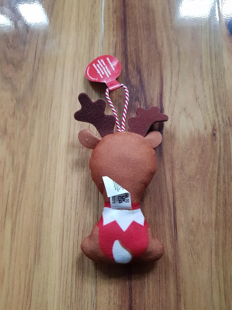 May include: A brown felt reindeer ornament with red antlers and a red and white Santa suit. The ornament has a white tag with the text "Gift your reindeer a friend!" and a red tag with the text "Made in China".