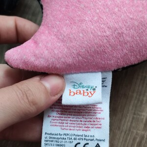 K&ouml;nnte beinhalten: Rosa-schwarzes Pl&uuml;schtier mit einem Disney Baby-Etikett. Das Etikett enth&auml;lt Pflegehinweise in mehreren Sprachen, darunter "Von Feuer fernhalten".