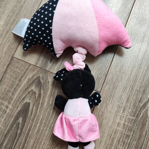 K&ouml;nnte beinhalten: Ein schwarzes und pinkfarbenes Pl&uuml;schtier mit einem rosa Regenschirm. Das Spielzeug hat einen schwarzen Kopf mit wei&szlig;en Punkten und einen rosa Rock mit wei&szlig;en Punkten.