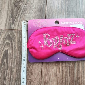 Pu&ograve; includere: Maschera per dormire in raso rosa con la parola "Bratz" in strass. La maschera &egrave; confezionata su una carta viola e bianca con le parole "Maschera per dormire" stampate su di essa.