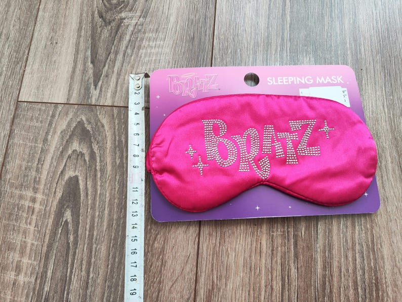 Pu&ograve; includere: Maschera per dormire in raso rosa con la parola "Bratz" in strass. La maschera &egrave; confezionata su una carta viola e bianca con le parole "Maschera per dormire" stampate su di essa.