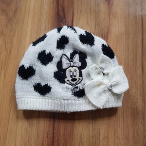 May include: White knit hat with black polka dots and a Minnie Mouse design. The hat has a white bow with a rhinestone accent.