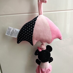 K&ouml;nnte beinhalten: Rosa-schwarzes Babyspielzeug mit einer Minnie Mouse Figur, die an einem rosa-wei&szlig; gepunkteten Regenschirm h&auml;ngt.