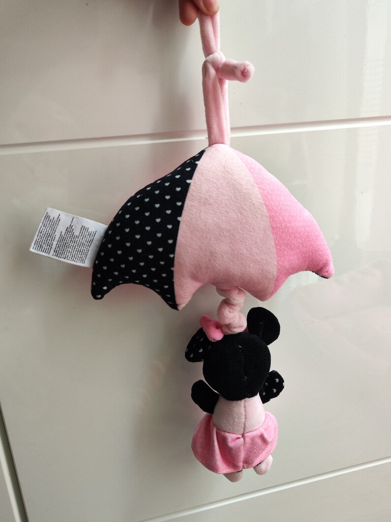 K&ouml;nnte beinhalten: Rosa-schwarzes Babyspielzeug mit einer Minnie Mouse Figur, die an einem rosa-wei&szlig; gepunkteten Regenschirm h&auml;ngt.