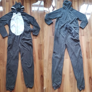 Może przedstawiać: Dwa szare piżamy typu onesie z motywem wilka. Jeden ma biały brzuch i kaptur z wilczą twarzą. Drugi to jednolity szary onesie z kapturem i ogonem.