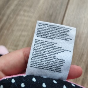 K&ouml;nnte beinhalten: Ein wei&szlig;es Etikett mit schwarzem Text, das Pflegehinweise f&uuml;r ein Produkt enth&auml;lt. Der Text umfasst Waschanweisungen in mehreren Sprachen, darunter Englisch, Spanisch, Deutsch, Franz&ouml;sisch, Italienisch, Polnisch und Portugiesisch. Das Etikett enth&auml;lt auch Anweisungen zur Reinigung des Produkts bei Flecken.