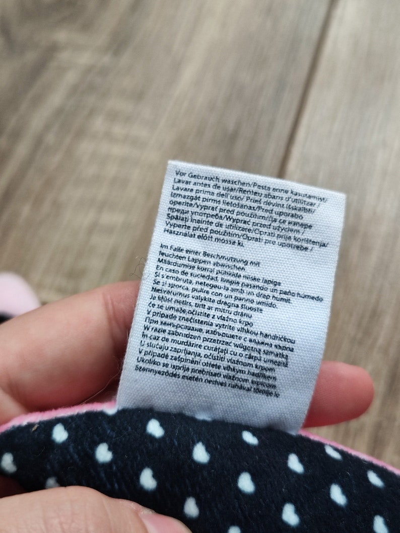 K&ouml;nnte beinhalten: Ein wei&szlig;es Etikett mit schwarzem Text, das Pflegehinweise f&uuml;r ein Produkt enth&auml;lt. Der Text umfasst Waschanweisungen in mehreren Sprachen, darunter Englisch, Spanisch, Deutsch, Franz&ouml;sisch, Italienisch, Polnisch und Portugiesisch. Das Etikett enth&auml;lt auch Anweisungen zur Reinigung des Produkts bei Flecken.