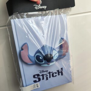 Może przedstawiać: Niebieski notes z postacią Stitch w 3D na okładce. Notes ma napis "Disney Stitch" na okładce.