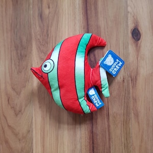 Peut inclure: Jouet en peluche en forme de poisson rayé rouge et vert avec un œil blanc et une étiquette bleue qui dit "Cuddle Crew".