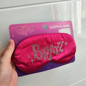 Pu&ograve; includere: Maschera per dormire in raso rosa con la parola "Bratz" in strass. La maschera &egrave; confezionata su una carta viola e bianca con le parole "Sleeping Mask" stampate su di essa.