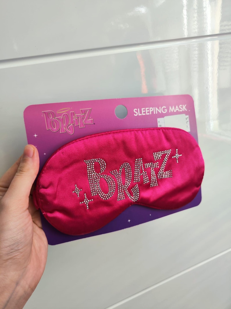 Pu&ograve; includere: Maschera per dormire in raso rosa con la parola "Bratz" in strass. La maschera &egrave; confezionata su una carta viola e bianca con le parole "Sleeping Mask" stampate su di essa.