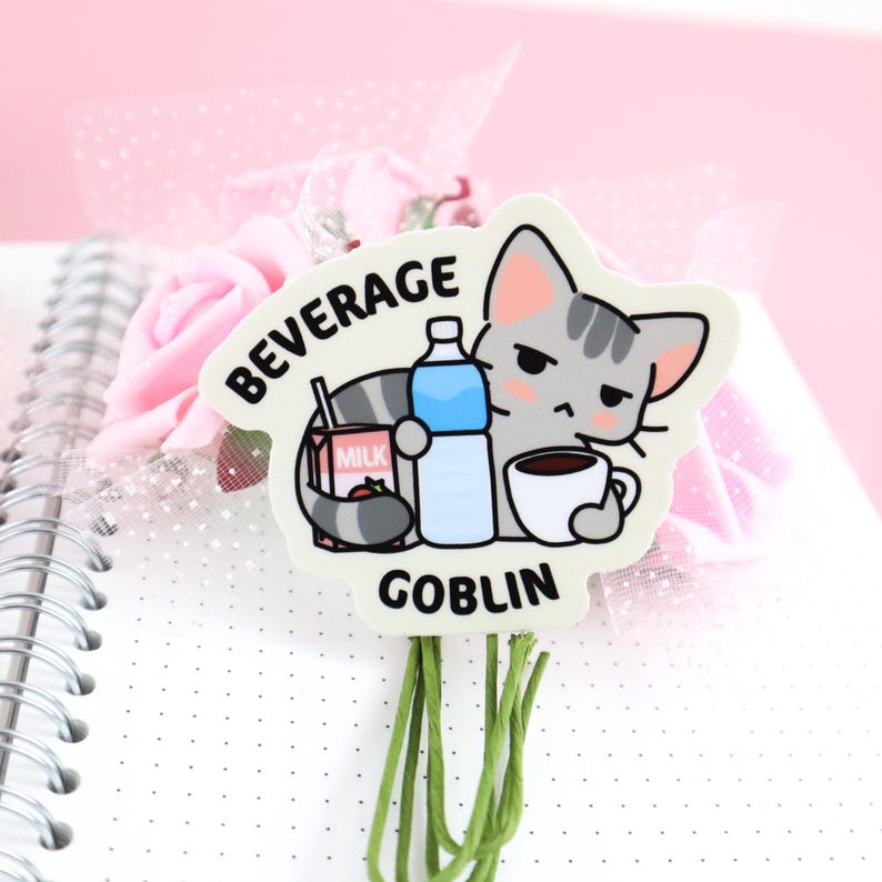 May include: A white sticker with a cartoon gray cat holding a cup of coffee, a carton of milk, and a bottle of water. The text "BEVERAGE GOBLIN" is printed on the sticker.