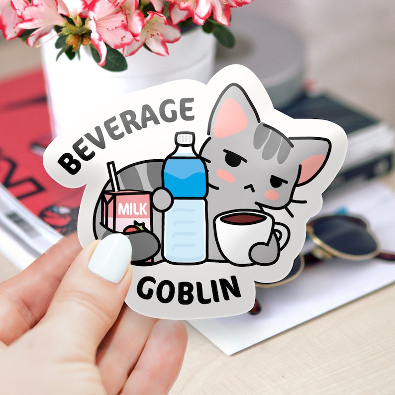 May include: A white sticker with a cartoon gray cat holding a cup of coffee, a carton of milk, and a bottle of water. The text "BEVERAGE GOBLIN" is printed on the sticker.