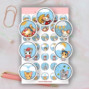 May include: A sheet of planner stickers featuring cartoon cats in various weather conditions. Each sticker is a circle with a blue background and a different cat illustration, including cats with sunglasses, umbrellas, and hats. The text "KITTIE TREATS SHOP" is at the bottom.