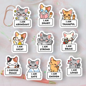 May include: Nine colorful stickers featuring cartoon cats with positive affirmations. Each sticker has a white border and features a different cat with a different affirmation. The affirmations include "I am abundant", "I am smart", "I am thankful", "I am lucky", "I am strong", "I am brave", "I choose peace", "I am safe", "I am enough", and "I am loved".