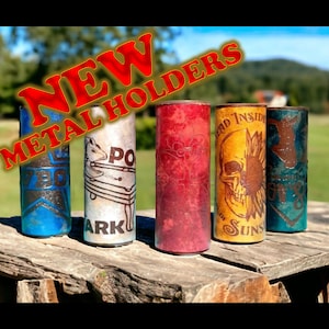 May include: Five metal can holders with different designs. The designs include a pool table, a skull with a sunflower, a star, a red swirl pattern, and a blue and brown design. The text "NEW METAL HOLDERS" is written in red letters across the top of the image.