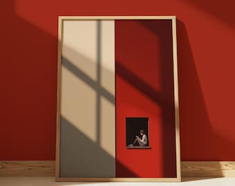 May include: A framed art print with a minimalist design. The background is split into beige and red sections. A small, dark window shows a person reading. The frame is light wood, and the artwork leans against a red wall.