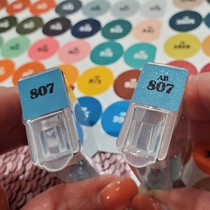 May include: Two small, clear plastic containers with blue lids. The lids have the number "807" printed on them. One lid has the letter "AB" printed above the number.