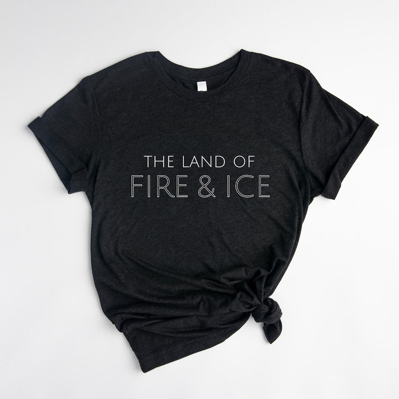 Op de afbeelding: Een donkergrijs T-shirt met de tekst "THE LAND OF FIRE & ICE" in wit gedrukt op de voorkant.