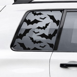 May include: Black bat window decals applied to a car window. The decals are in various sizes and orientations, creating a spooky Halloween theme. The car is white, and the window is tinted.