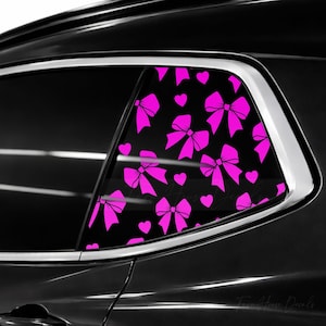 May include: A car window decal featuring a repeating pattern of bright pink bows and small hearts against a black background. The adhesive graphic is applied to the glass of a vehicle window, displaying a vibrant contrast between the pink shapes.