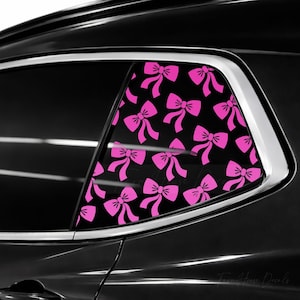 May include: A car window decal featuring a repeating pattern of bright pink bows against a solid black background. The decal is applied to the rear side window of a black vehicle, covering the glass surface with a decorative bow motif.