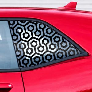May include: A red car window featuring a black and grey geometric decal with a repeating hexagonal pattern. The decal covers the entire surface of the rear side window, creating a bold, high-contrast visual effect against the bright red vehicle body.