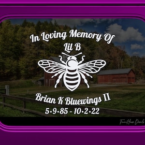 May include: A white decal with the text "In Loving Memory Of Lil B" and "Brian K Bluewings II 5.9.85 - 10.2.22" is displayed on a window. A large white bee graphic is centered between the text. The background shows a rural landscape with trees and buildings.