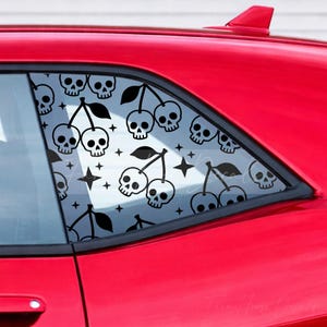 May include: A black vinyl car window decal featuring a repeating pattern of cherries where the fruit is replaced by skulls. The design includes small four-pointed stars interspersed between the skull-cherries on the red car window surface.