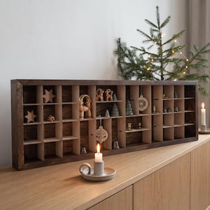 May include: A rectangular dark brown wooden display shelf with multiple square compartments. The shelf contains various small decorative items including wooden stars, miniature figurines, and ornaments. The structure is made of dark wood.