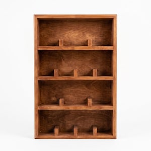 Peut inclure: Étagère d'exposition rectangulaire en bois brun foncé. Elle comporte quatre étagères, chacune avec deux petits supports verticaux. L'étagère est conçue pour contenir de petits objets et est posée sur un fond blanc. Mesures en cm.